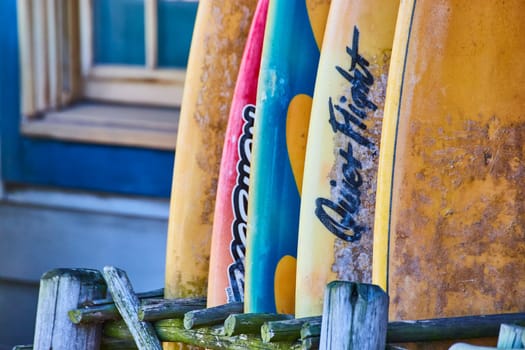 Colorful used surfboards stacked against a rustic fence, evoking seaside adventures and coastal charm.