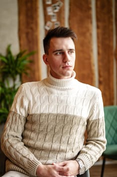 A man sitting comfortably in a chair, wearing a cozy sweater. He appears relaxed and content in a casual setting, with a warm ambiance.