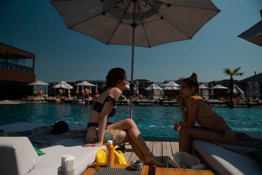 A duo of friends in swimwear enjoy a leisurely afternoon by the poolside. High quality photo