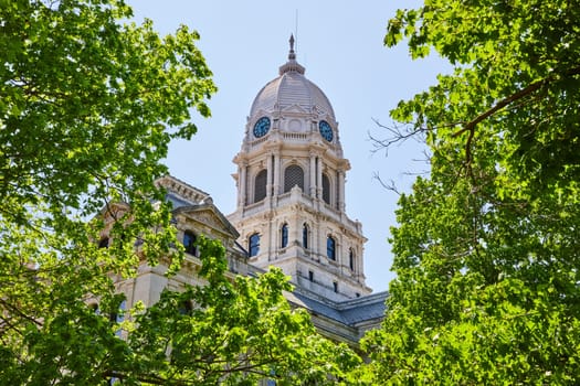 Historic Kosciusko County Courthouse with ornate dome, framed by lush greenery under a clear blue sky.