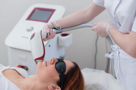 Close-up of laser hair removal on a woman's face. The doctor removes unwanted hair from the patient above the lip with an electric device.