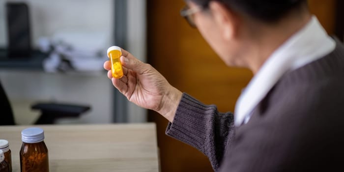 Senior asian man examining prescription medication at home.