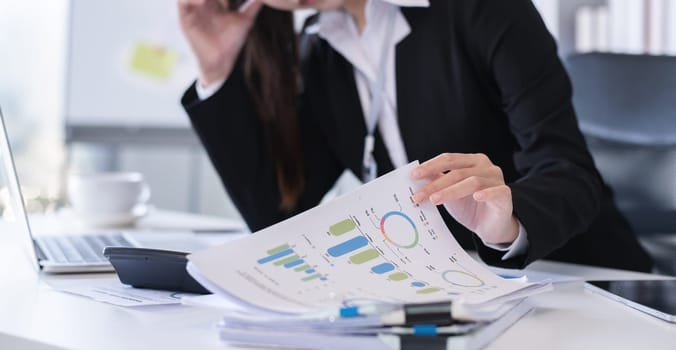 Accountant sitting with financial documents, using laptop, calculating financial and tax figures for company on table in office.