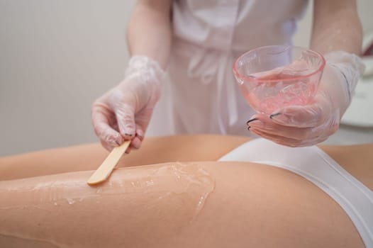 The master applies the anesthetic gel with a spatula to the woman's legs before laser hair removal. Permanent hair removal with a device in the clinic.