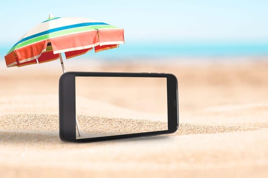 Mobile phone screen with beach umbrella on the sandy beach with blue sky background.
