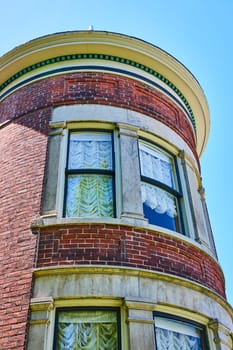 Elegant vintage brick turret with ornate windows under a clear blue sky, in Fort Wayne's historic district.