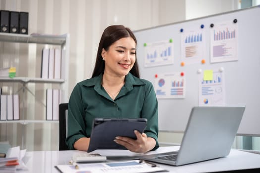 Asian businesswoman working on financial document with laptop on desk in office room.