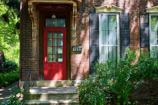 Charming vintage home in Fort Wayne with a striking red door, nestled in lush greenery, evokes tranquility and privacy.