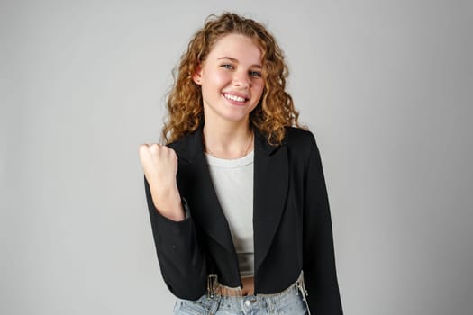 Excited Young Woman Celebrates Success With Raised Fists Against a Gray Background in studio