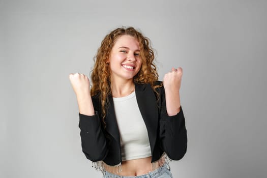 Excited Young Woman Celebrates Success With Raised Fists Against a Gray Background in studio