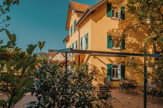 Image of a empty coffee tables arranged in backyard of a house. Autumn in Germany, Europe. Outdoor table in street cafe. autumn outdoor cafe wooden furniture old europe. Autumn photo of old-fashioned cozy and empty outdoor cafe with wooden furniture in a European town. Cafe concept