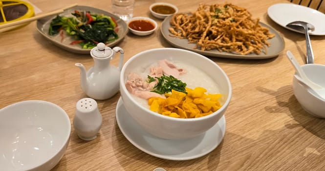 rice porridge with shredded chicken called bubur ayam served with crackers and sliced spring onion and others condiments in restaurant