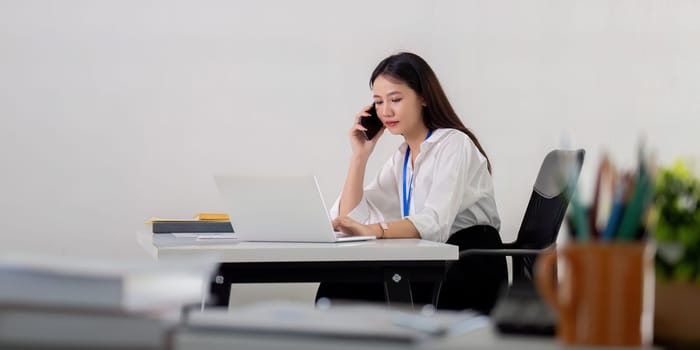 Professional Asian Businesswoman Making Phone Call at Modern Office Desk.