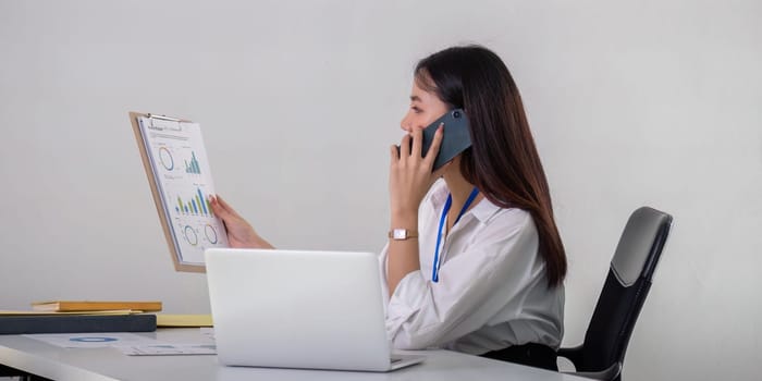 Asian Businesswoman Discussing Data Analysis Over Phone in Office Setting.