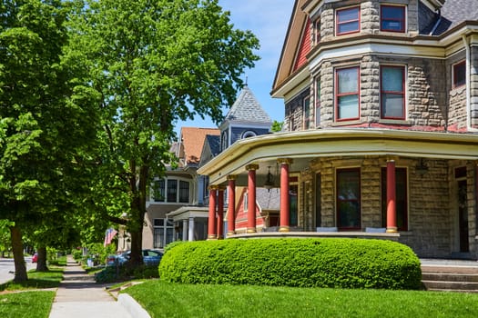 Historic stone house with red columns in a lush, suburban Fort Wayne neighborhood under clear skies.