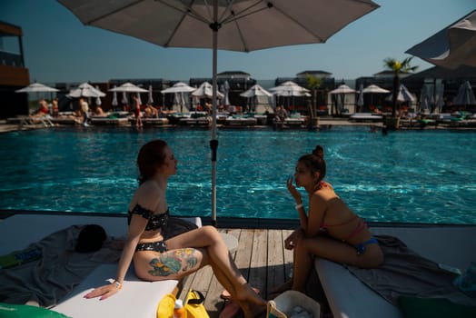 Two friends in bathing suits chat happily as they sit beside the pool. High quality photo