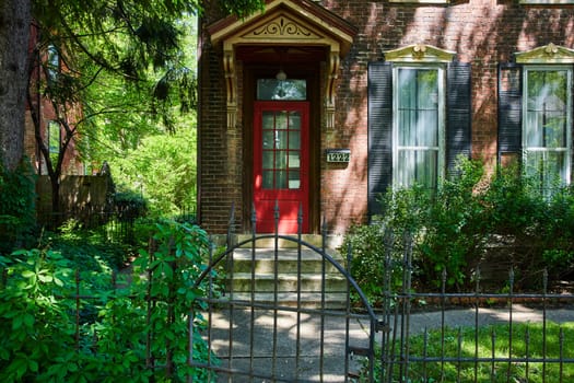 Traditional red door entrance of a brick house in Fort Wayne, framed by lush greenery and historic charm.