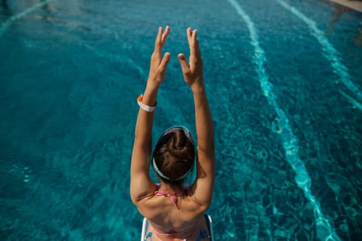 A stunning lady in a bikini reclines by the poolside, her back turned to the water. High quality photo