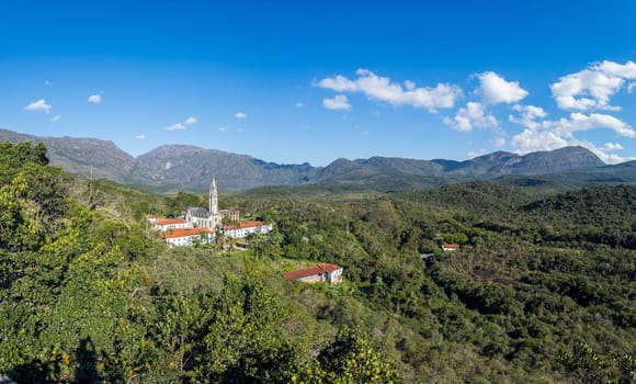 Historic church stands out amid forests and mountains under a blue sky, Caraca in Brazil