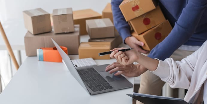 A happy Asian online shopping entrepreneur couple takes orders and packs products to send to customers together in their office..