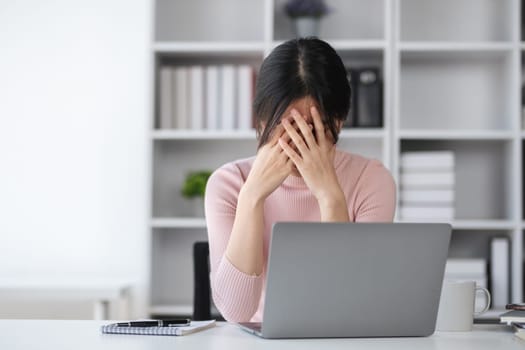 Young woman is dizzy and stressed while working online on her laptop at home..