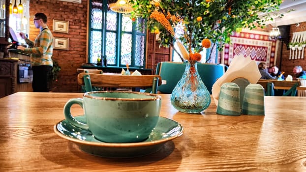 A ceramic teacup rests on a table with cafe interior in soft focus behind