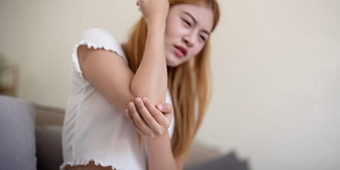 Young woman feeling pain in her elbow while sitting indoors.