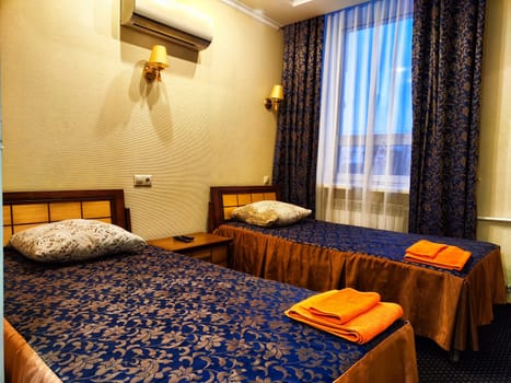 Twin Beds in Cozy Hotel Room. Two single beds with blue bedding and orange towels in a hotel room