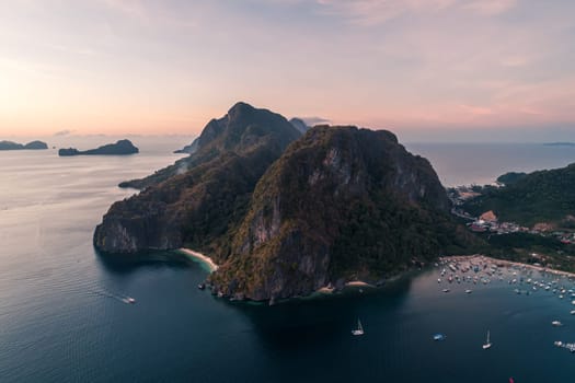 Aerial view of cliffs in the sea, yachts are sailing nearby, mountains covered with tropical forest. Aerial view of the gorgeous tropical mountains and the ocean.