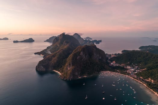 Aerial view of cliffs in the sea, yachts are sailing nearby, mountains covered with tropical forest. Aerial view of the gorgeous tropical mountains and the ocean.