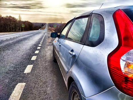 The car is on the side of the road. The concept of travel. A silver car stopped by the highway as daylight breaks