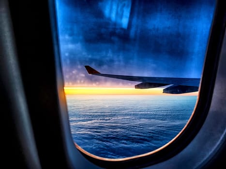 Airplane wing, clouds and sunrise through plane window. Wing silhouetted against vibrant sky and clouds. Sunset Horizon View From Airplane. Blurred