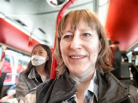 Hong Kong, China - April, 05, 2024: Smiling woman with fellow commuters on a red Hong Kong bus