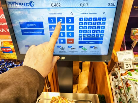 Kirov, Russia - April 17, 2024: Customer Weighing Produce on Digital Scales at Grocery Store. A person is using a touchscreen to weigh items at store