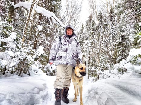 Adult girl or mature lady with shepherd dog in winter nature landscape in forest. Middle aged woman training big shepherd dog in cold day. Friendship, love, communication, fun, hugs