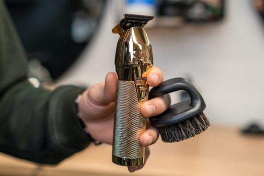 Hairdresser holding trimmer and brush in the hand in barbershop.