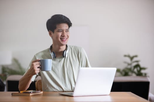 Young Asian student doing homework and studying online, online video call on laptop happily at home.