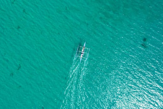 Aerial top view of Banca boat floating in open sea with clear and turquoise water on sunny day . Tropical landscape.