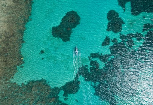 Aerial top view of Banca boat floating in open sea with clear and turquoise water on sunny day . Tropical landscape.