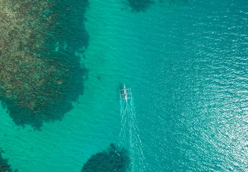 Aerial top view of Banca boat floating in open sea with clear and turquoise water on sunny day . Tropical landscape.