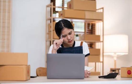 A small SME business owner feels tired while sitting on his home desk packing products into boxes..