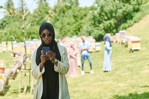 Middle Eastern Muslim woman in a hijab uses a smartphone while managing a small beekeeping business, blending modern technology with traditional practices