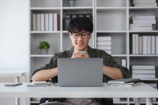 Young Asian student boy in private clothes studying online with laptop at home..