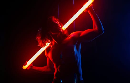 Sporty handsome man with neon light tube under colorful illumination, laser, smoke room. Muscular strong guy with naked torso abs. Projection illusion mapping. Futuristic model.