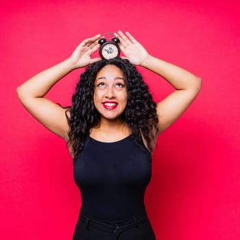 Smiling young african american woman posing isolated on a red background with clock