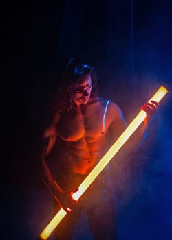 Sporty handsome man with neon light tube under colorful illumination, laser, smoke room. Muscular strong guy with naked torso abs. Projection illusion mapping. Futuristic model.
