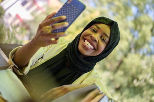 A serene African American Muslim woman in hijab engages in a peaceful conversation on her cellphone amidst the tranquil beauty of nature