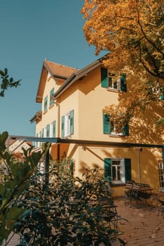 Image of a empty coffee tables arranged in backyard of a house. Autumn in Germany, Europe. Outdoor table in street cafe. autumn outdoor cafe wooden furniture old europe. Autumn photo of old-fashioned cozy and empty outdoor cafe with wooden furniture in a European town. Cafe concept