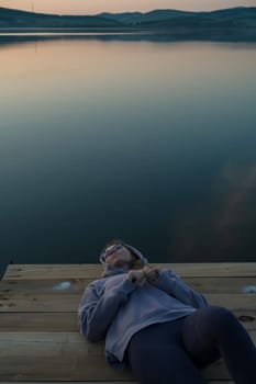 Woman lying down on the pier at lake, closeup portrait, summer sunset