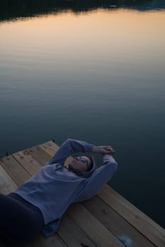 Woman lying down on the pier at lake, closeup portrait, summer sunset